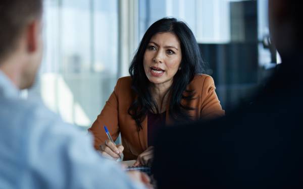 Person in a brown blazer holding a pen during a meeting in a modern office setting.