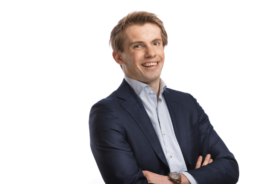 Person in a dark blue suit with a light blue shirt, arms crossed, wearing a wristwatch, and face blurred.