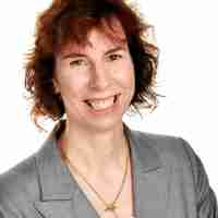 Person with curly hair in a gray blazer and gold necklace, face blurred.