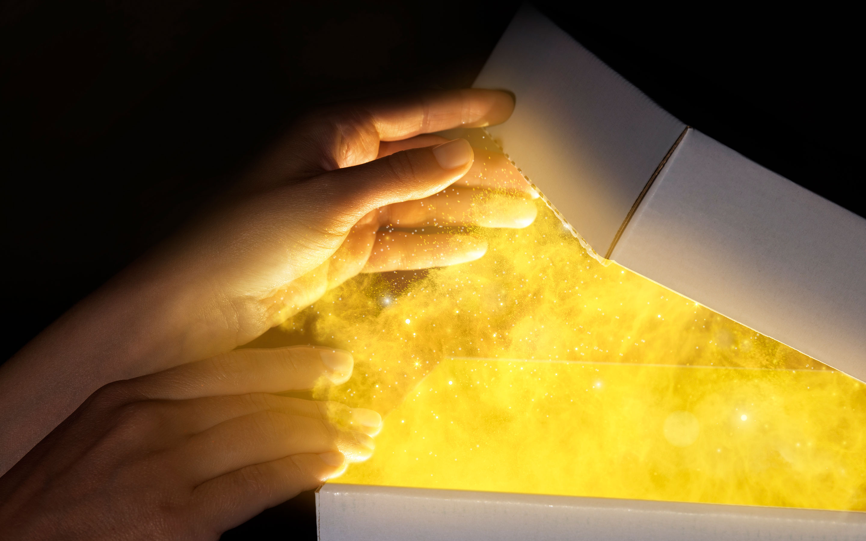 Hands holding an open book with a glowing, magical yellow substance emerging from its pages, surrounded by sparkles and light particles