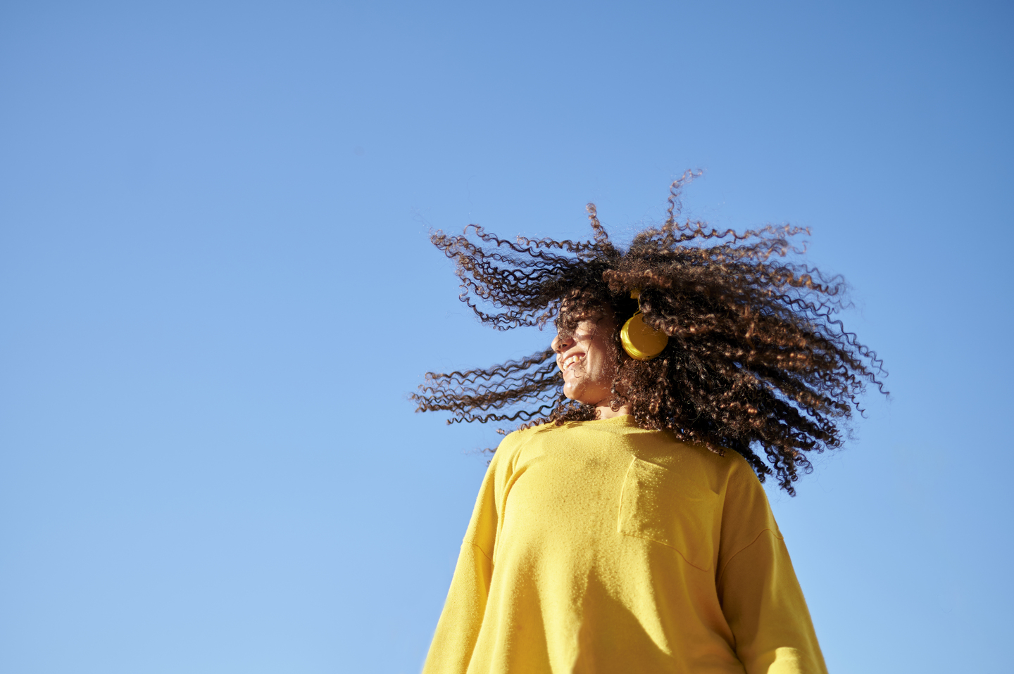 Woman moving her curly hair with blue sky in the background