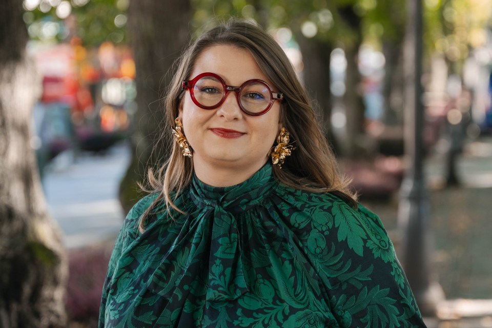 Portrait of Vitalija Bartuseviciute outdoors, wearing glasses and a green outfit, with trees in the background.