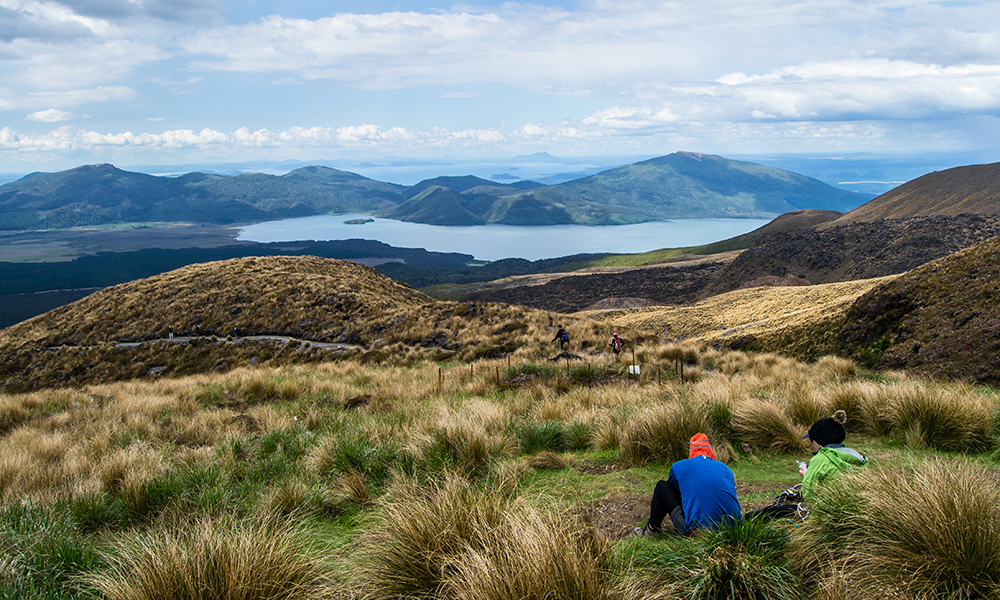 Two hikers looking at view of lake Rotoaira and lake Taupo from Tongariro Alpine Crossing hike with clouds above