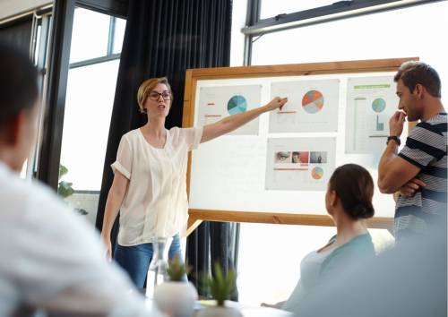 a woman is speaking to her colleagues from work in the conference room, pointind charts on the screen
