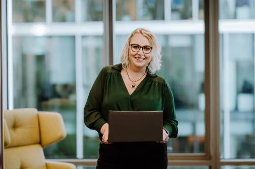 młoda kobieta uśmiechająca się na wprost kamery z laptopem w ręce