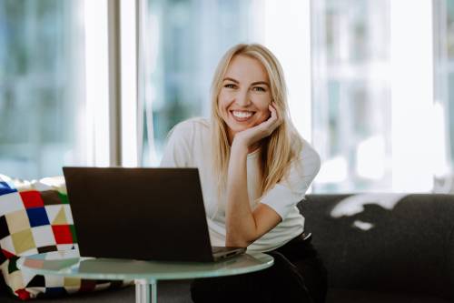 uśmiechnięta młoda kobieta siedząca przy latopie patrząca na wprost