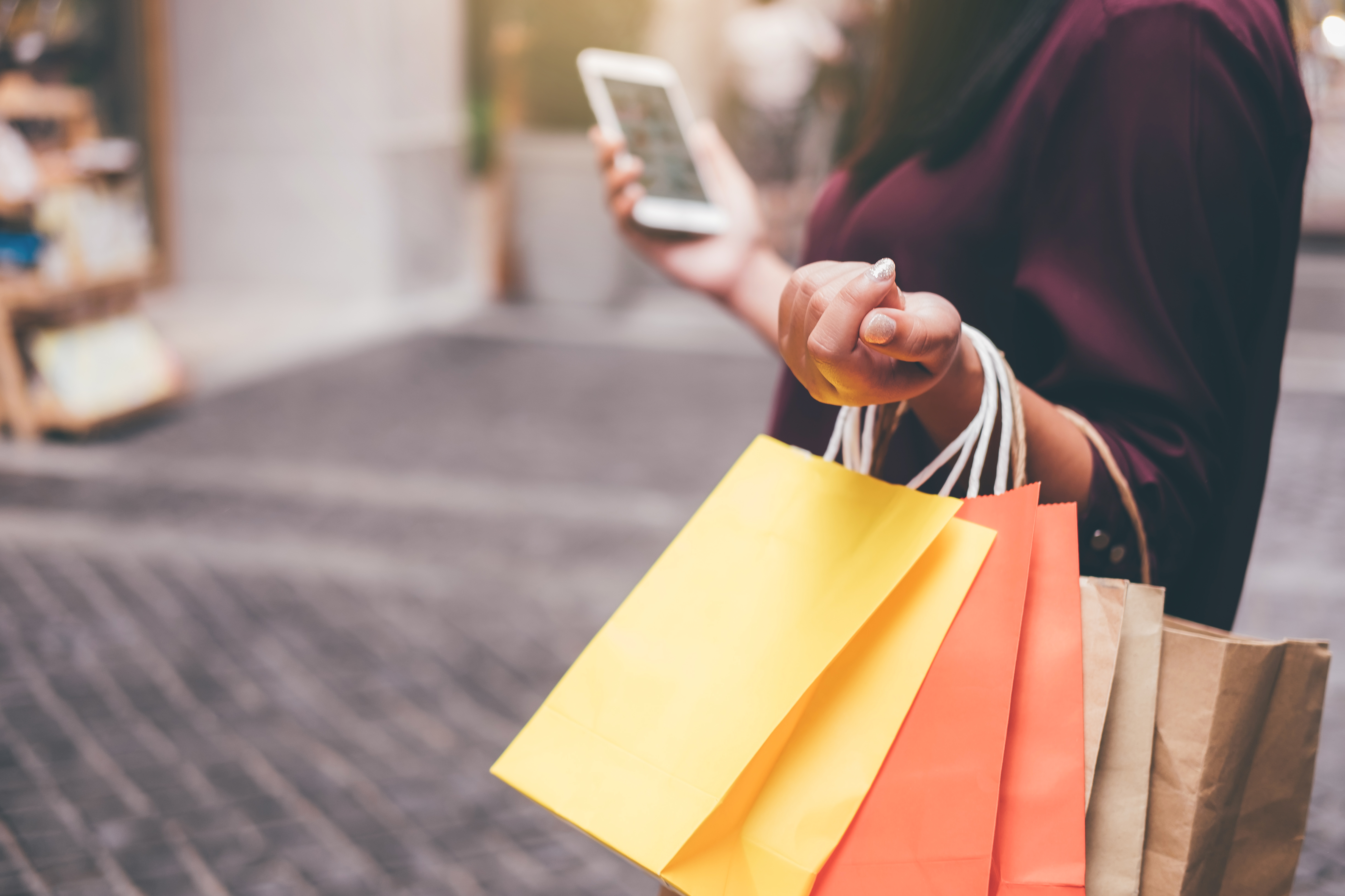 Midsection Of Woman Using Mobile Phone While Holding Shopping Bags