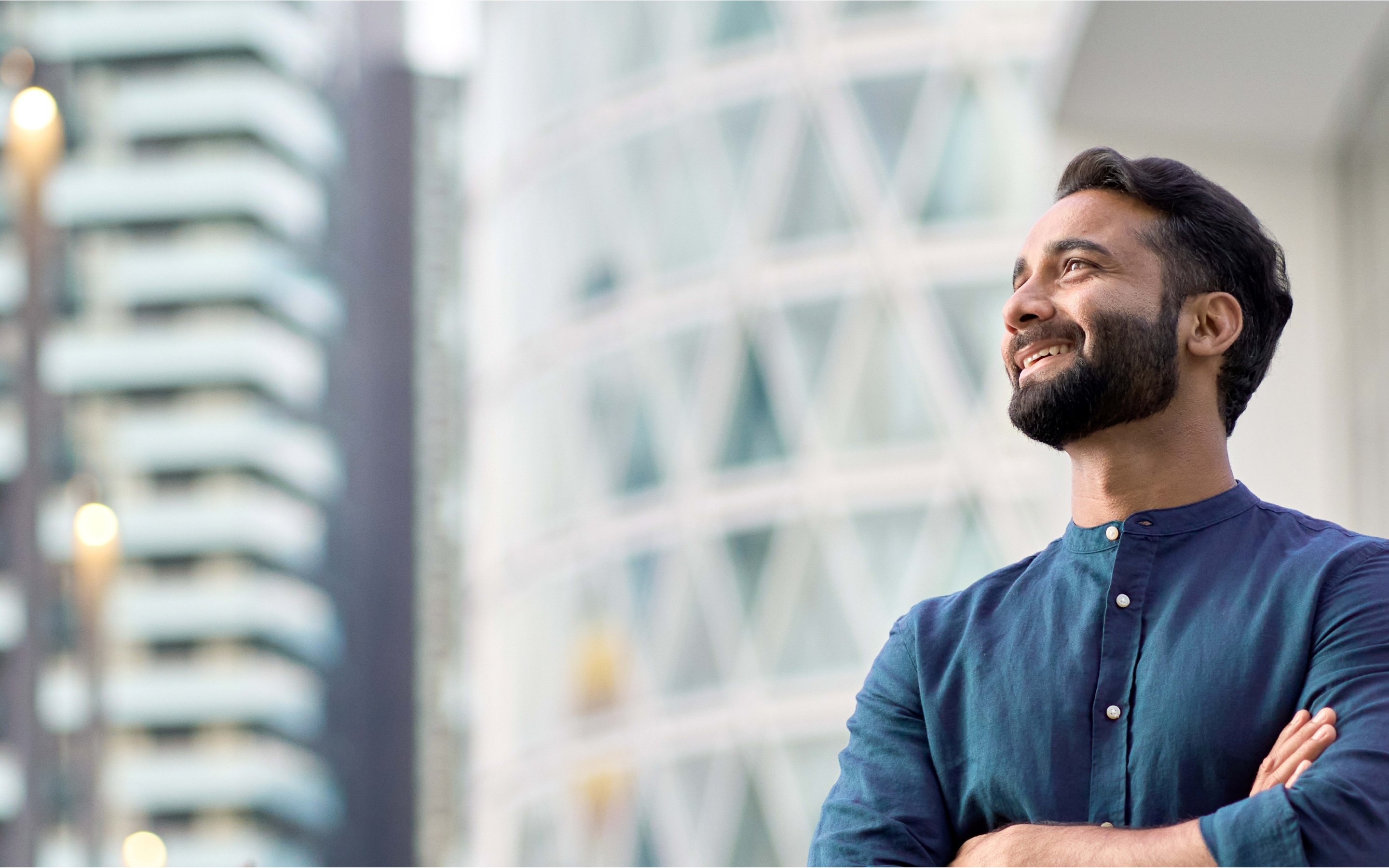 Person in a blue shirt standing outdoors with a modern glass-and-steel building featuring geometric patterns in the background.